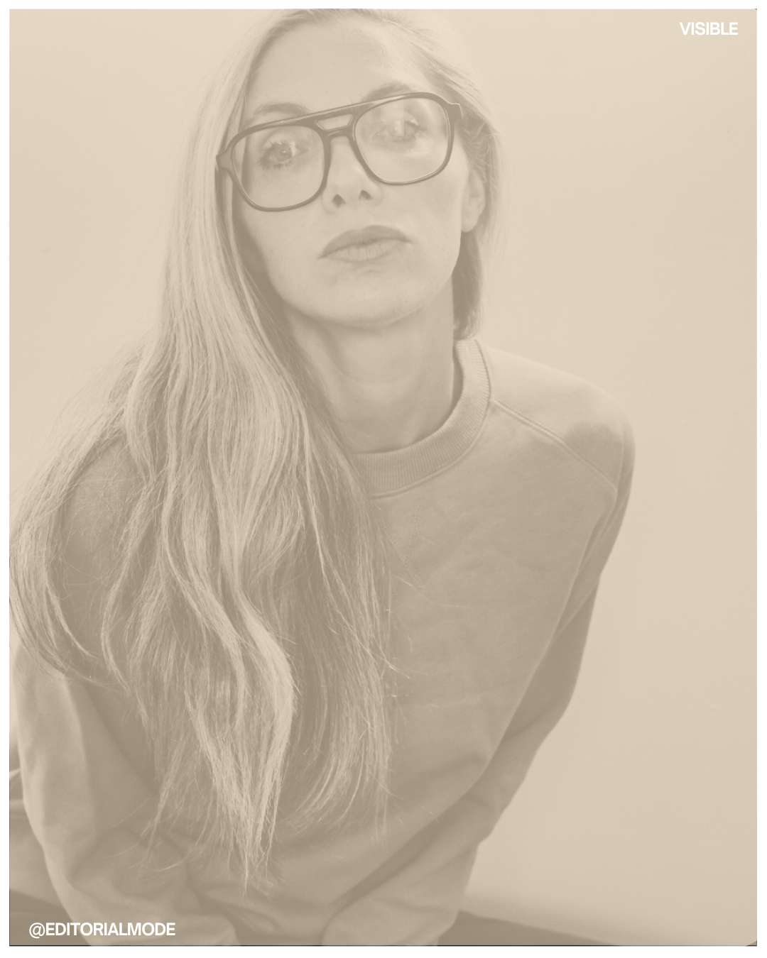 A woman with long wavy hair and glasses, wearing a sweatshirt, looking at the camera against a plain background.