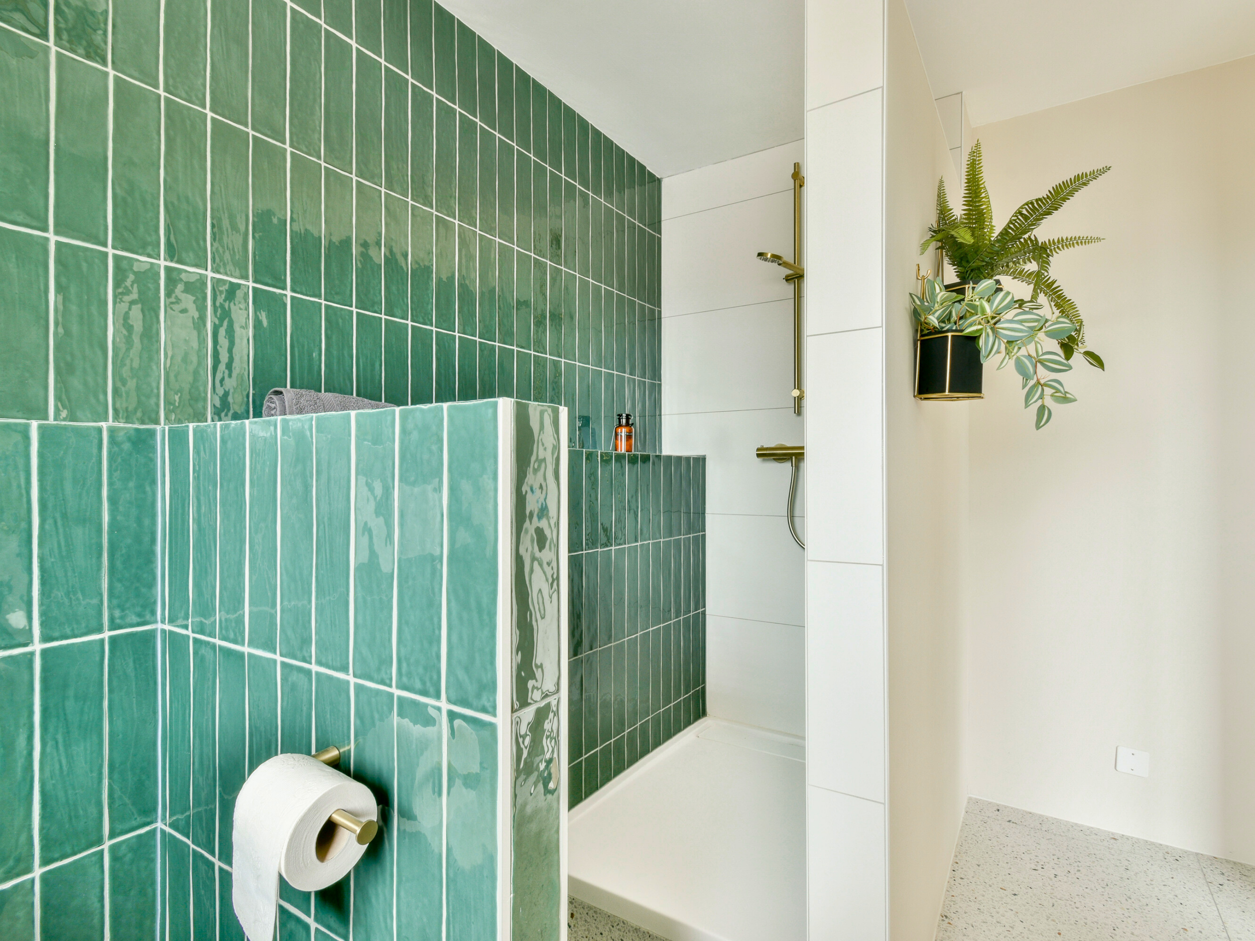 Modern bathroom shower area with green tiled wall, white tiles, and two potted plants hanging on the white wall.