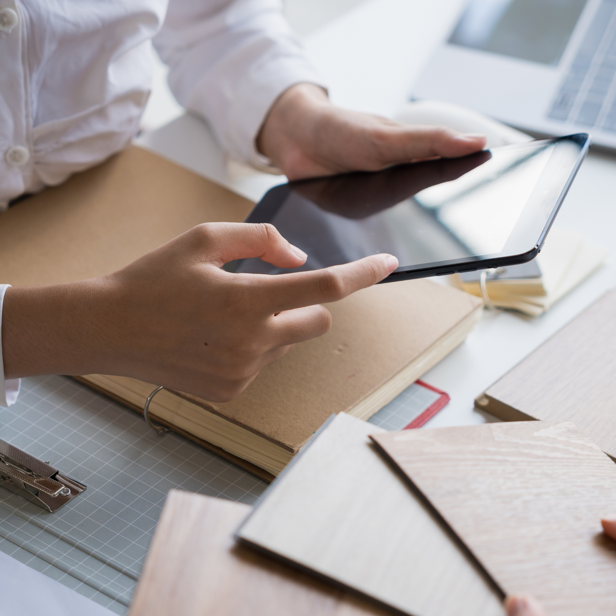 Person holding a tablet over a desk with books, notebooks, and color samples.