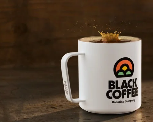 White coffee mug with a logo and the words "Black Coffee Roasting Company" next to a splash of coffee inside the mug.
