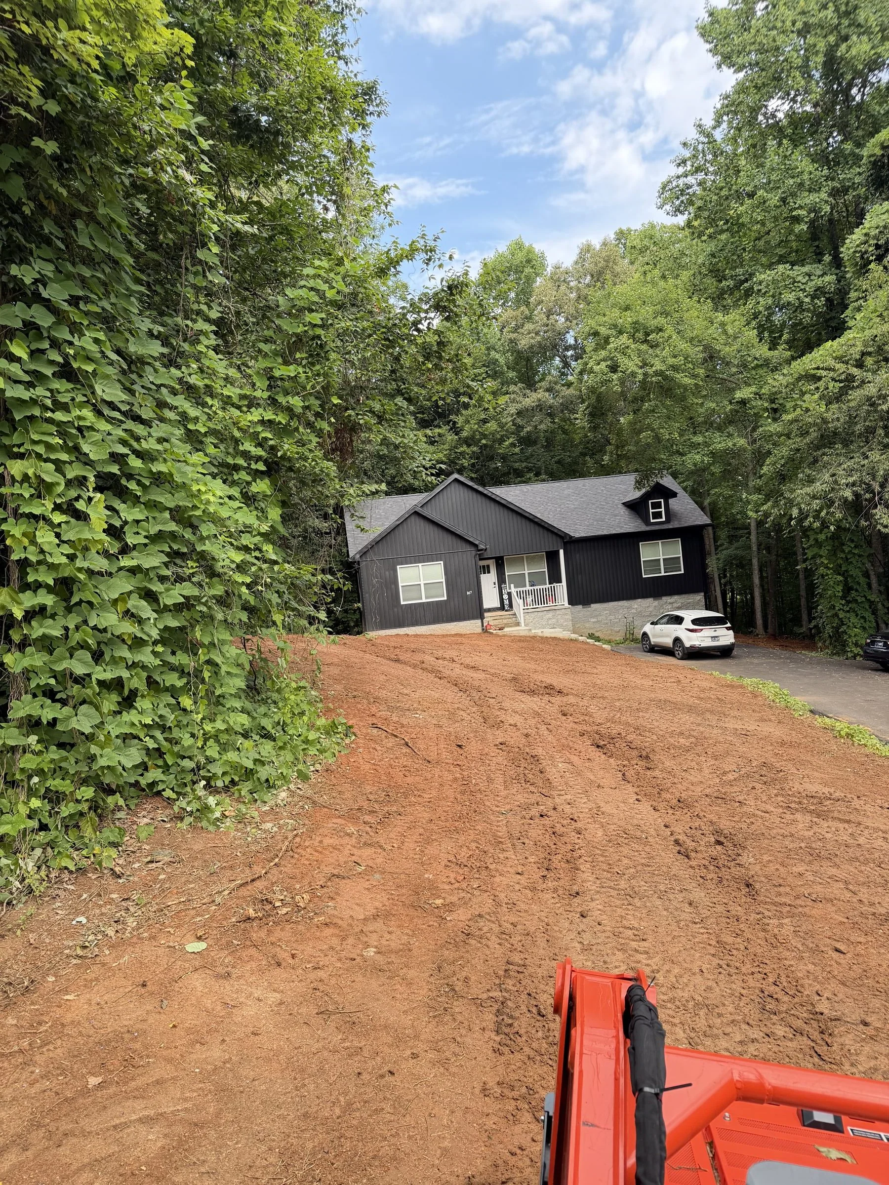 Skid steer grading a red clay dirt lot beside a home in DeKalb County, TN