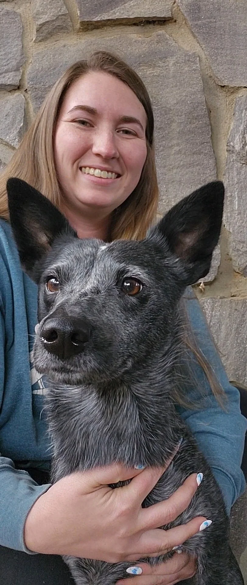 Lauren smiling in a photo with a well-groomed black and grey dog