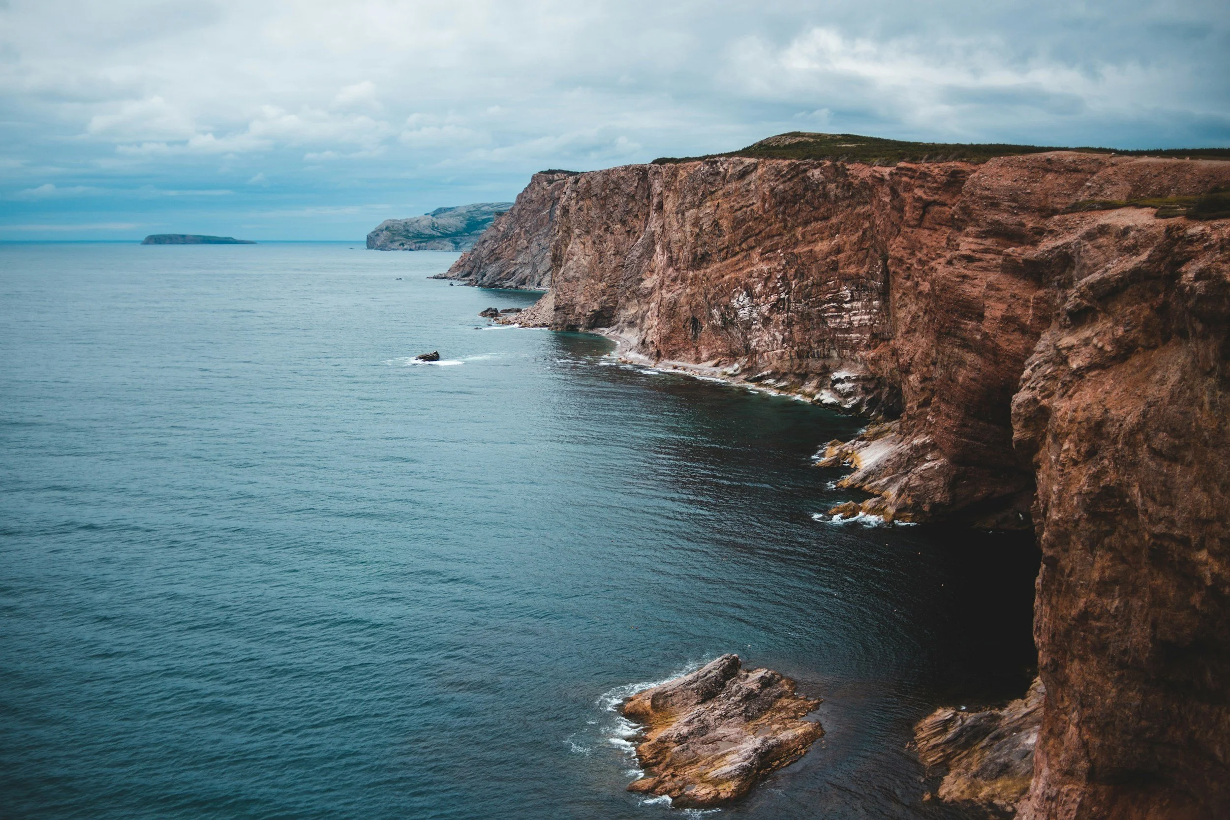 Cliffs along a coastline with ocean water and a cloudy sky.