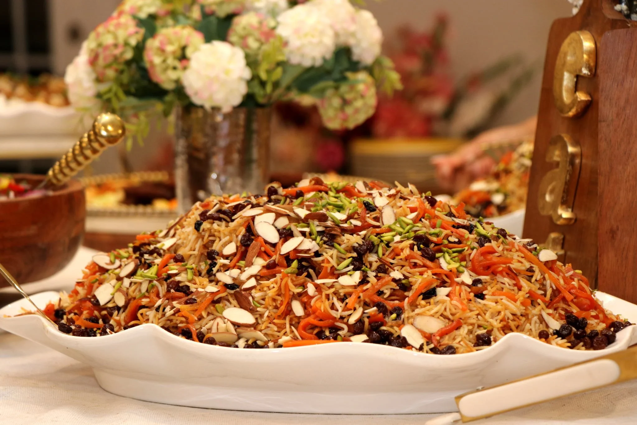 Colorful fried rice with vegetables and sliced almonds on a white serving dish at a festive gathering.