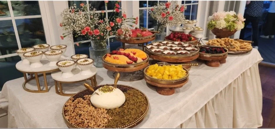 Dessert table with various sweets and fresh fruit, decorative flowers in vases, and a white tablecloth.