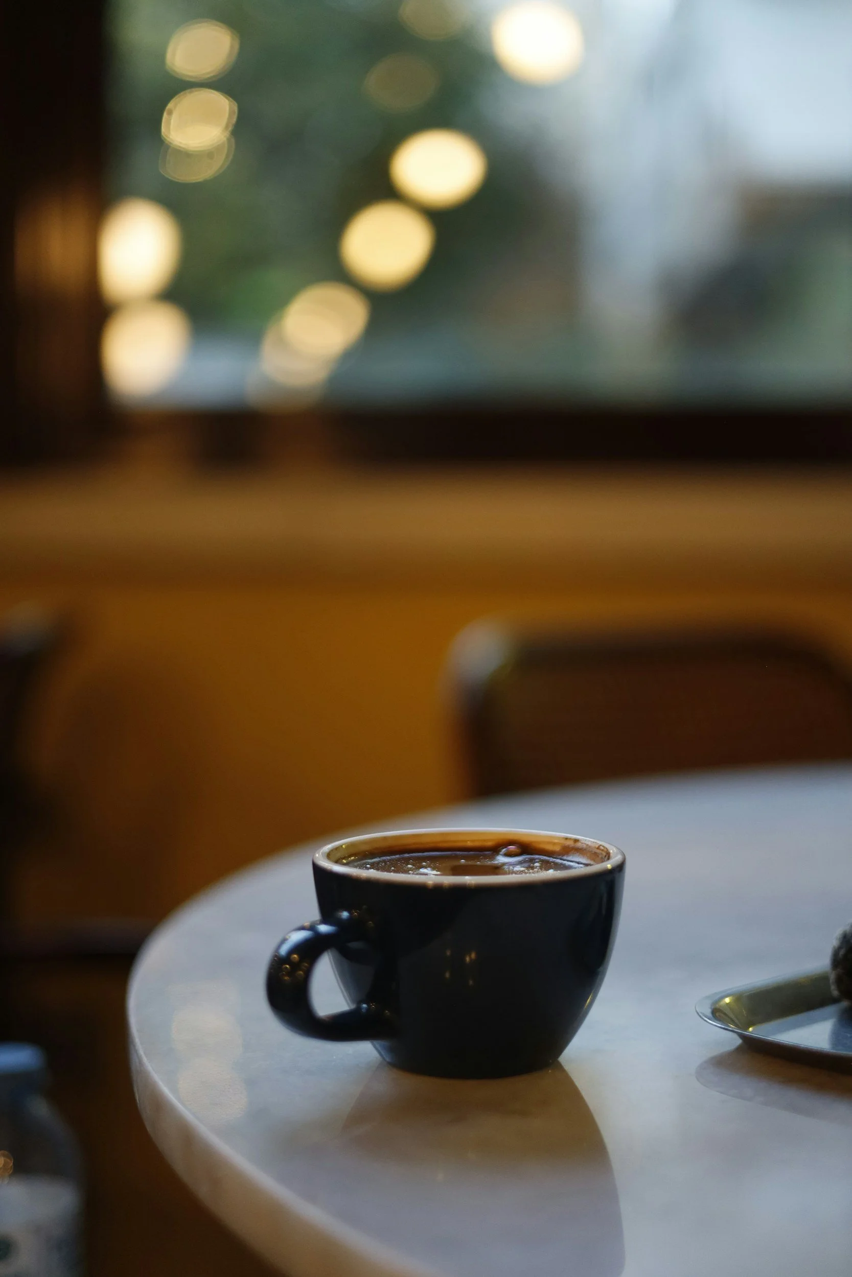 A warm, black coffee cup filled with coffee on a white table with a blurred background with glowing lights.