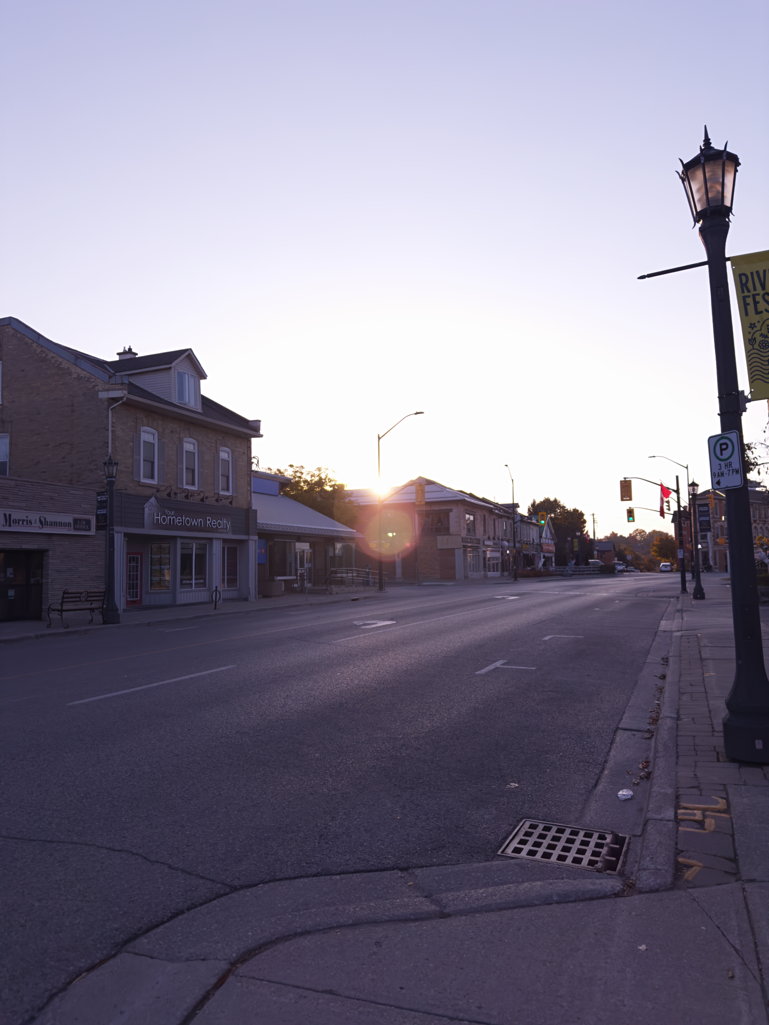 Empty street with storefronts, lamp posts, and a sunset in the background.