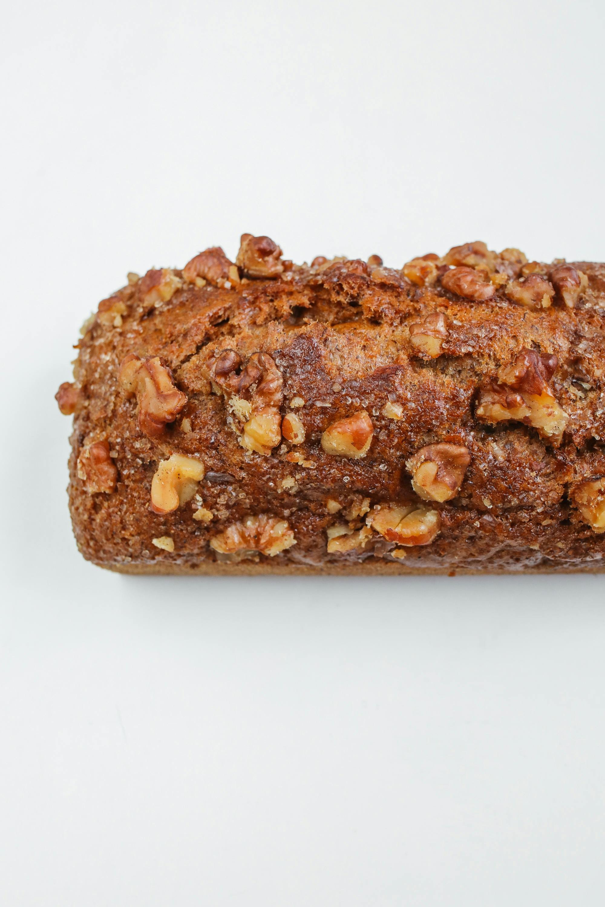 Close-up of a loaf of carrot cake with chopped walnuts on top, placed on a white surface.
