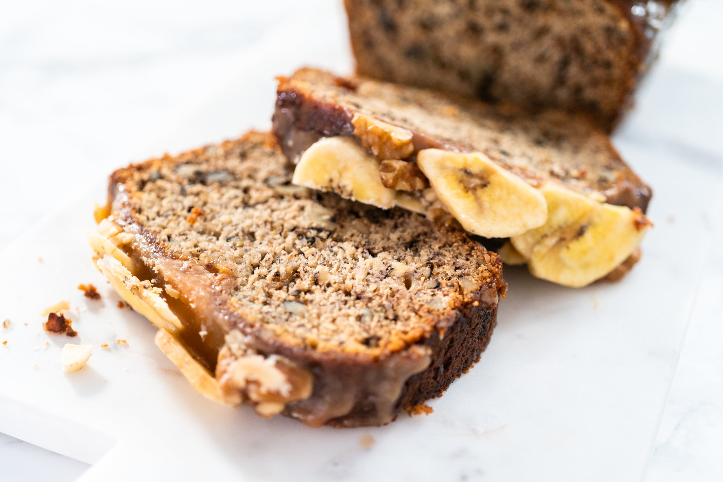 Close-up of a sliced banana nut bread with chopped nuts, placed on white parchment paper.