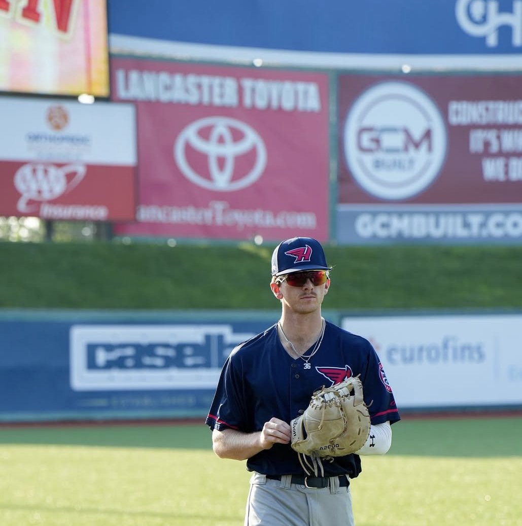 Bryce Cannon in a dark blue uniform with the logo of the Atlanta Braves, wearing sunglasses and a cap, stands on the field holding a baseball glove.
