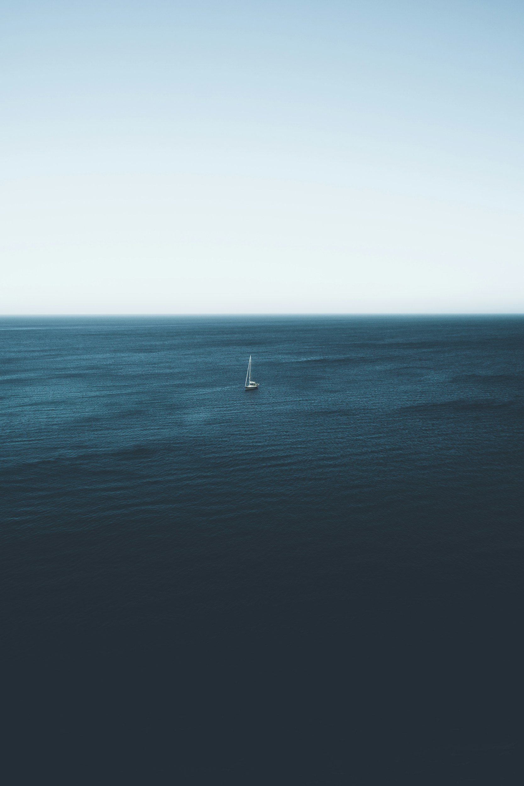 A sailboat floating on calm ocean waters under a clear sky.