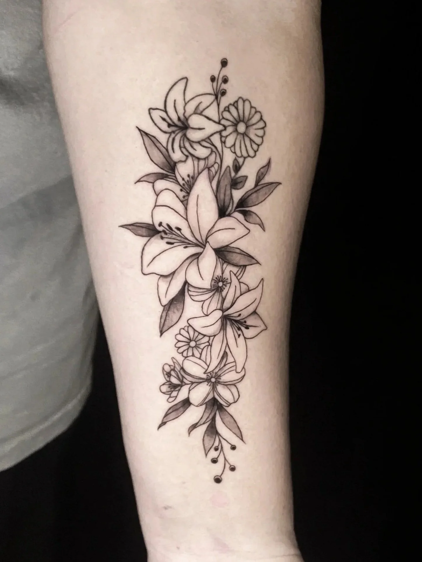 A black and gray floral tattoo on a person's forearm featuring lilies, daisies, and leaves. carlee tattoos carlee grace tattoo artist hoschton ga Georgia braslton winder homer commerce north geogria