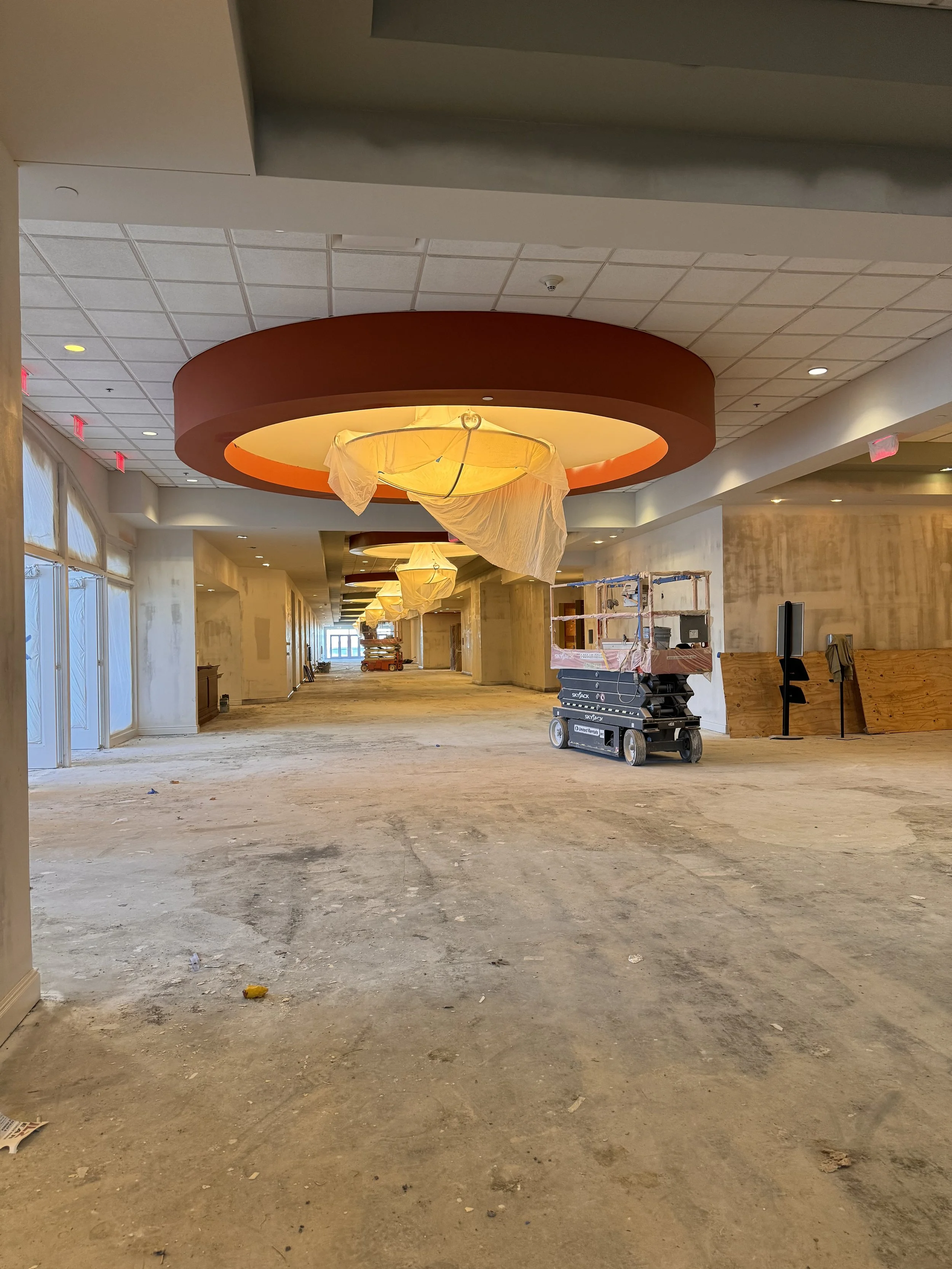 Interior of a building under construction with a partially finished floor, ceiling lights, and large decorative circular ceiling fixtures.