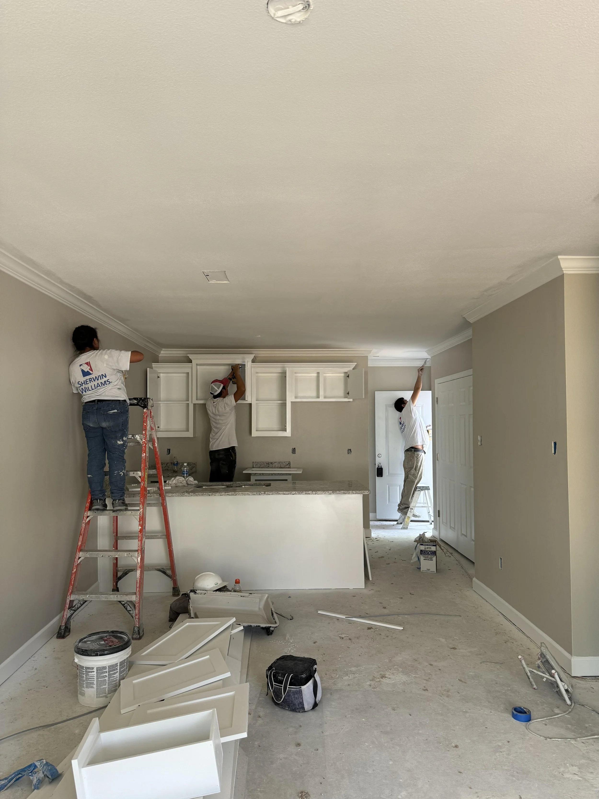 Three workers installing white kitchen cabinets in a new home.