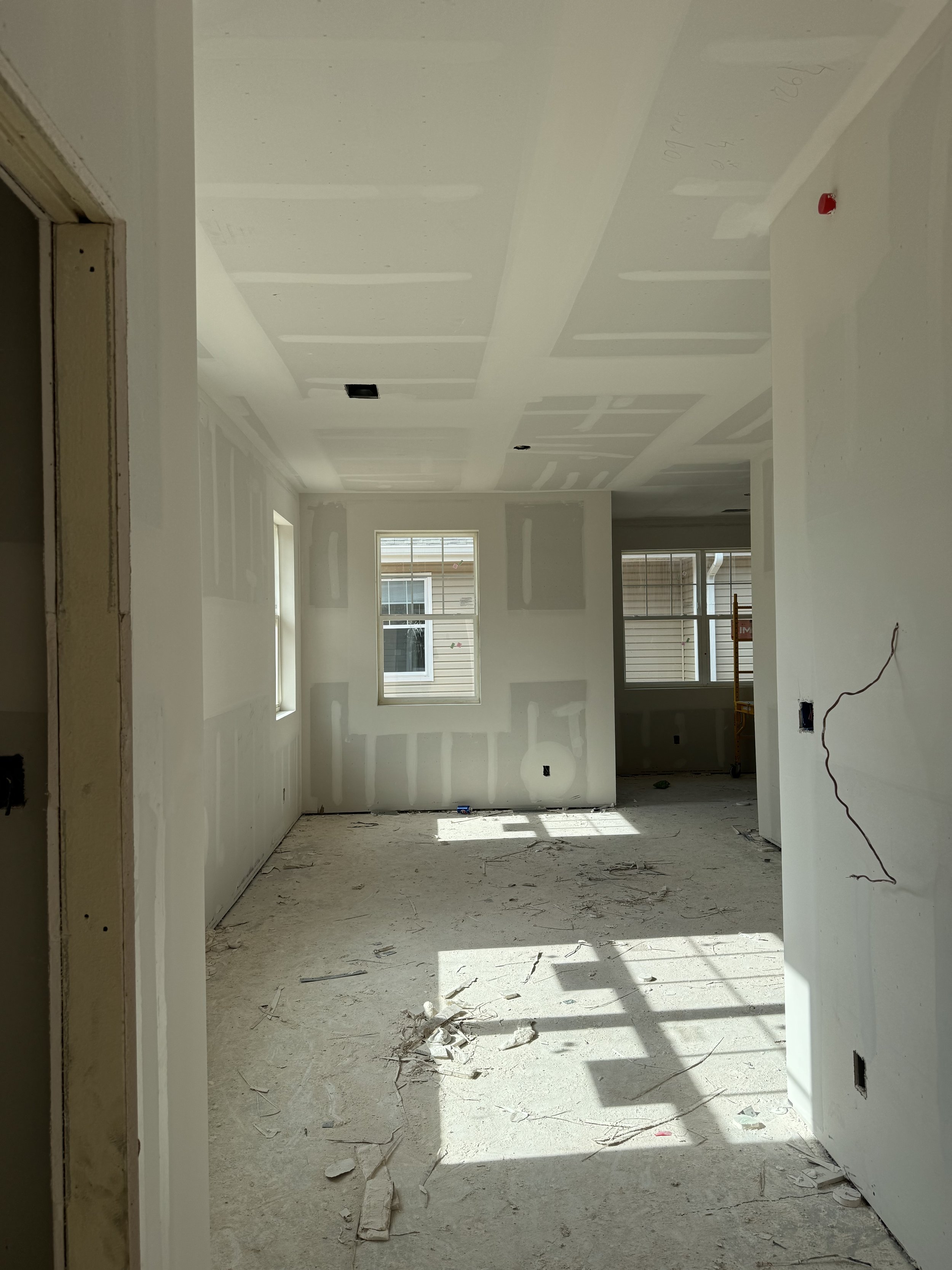 Interior of a house under construction with unfinished drywall, construction debris, and windows letting in natural light.