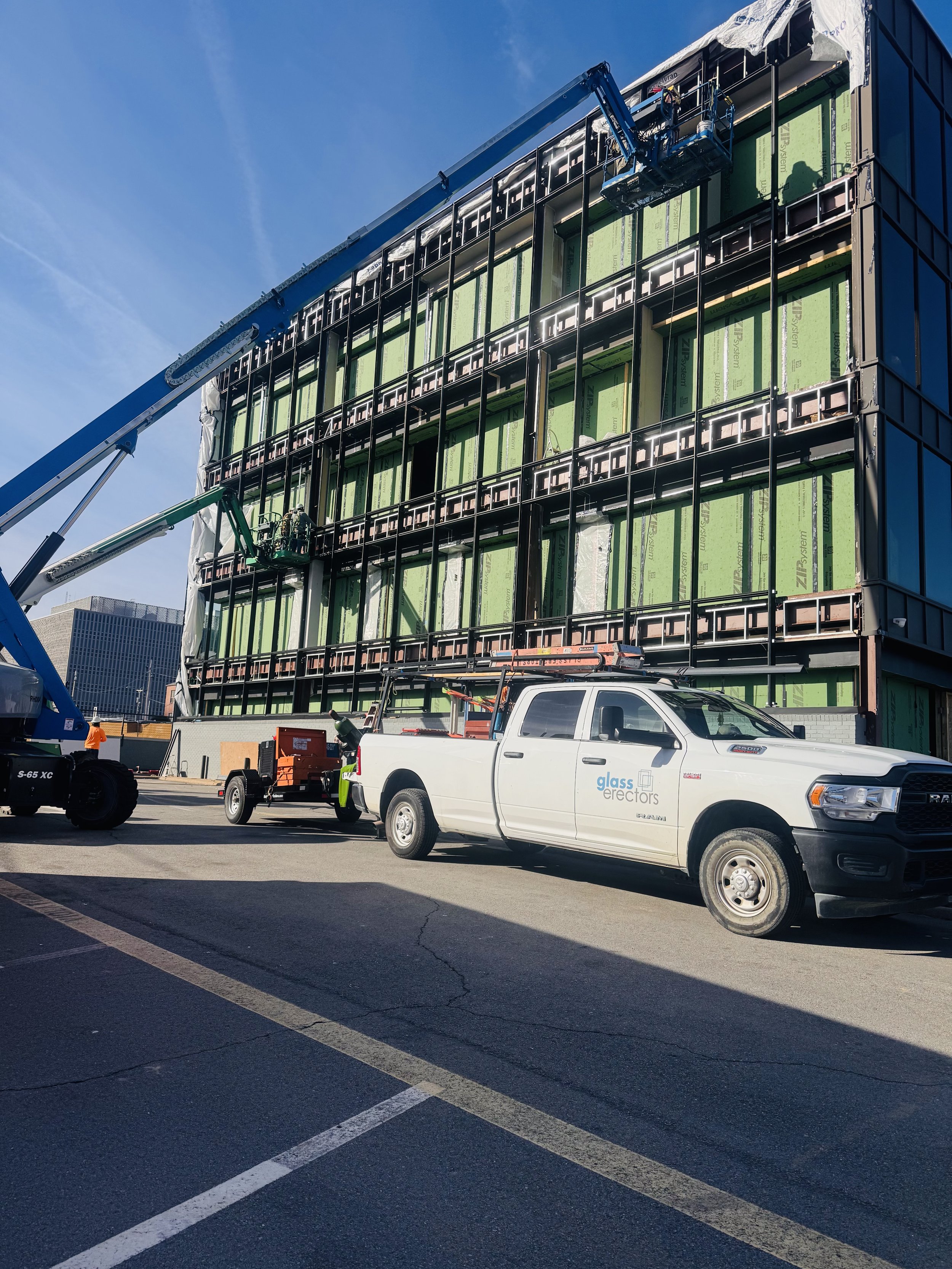 Construction workers install large glass windows on the exterior of a building using a crane and lift equipment.