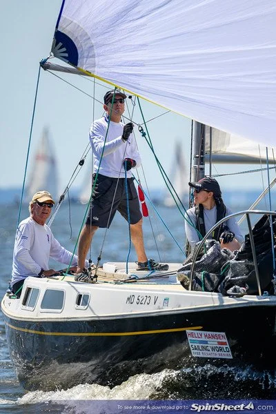 Three people sailing on a boat with a large sail in open water.