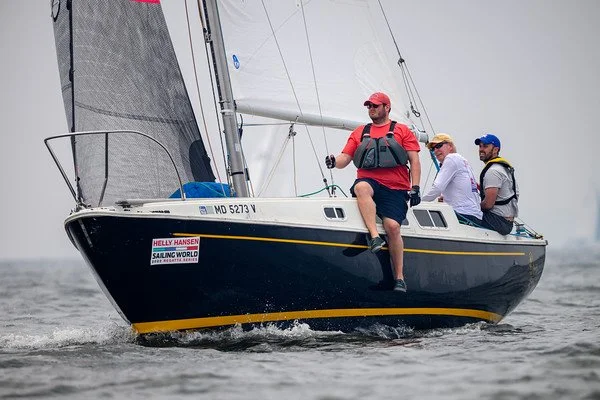 Three people sailing on a small black sailboat on the water.