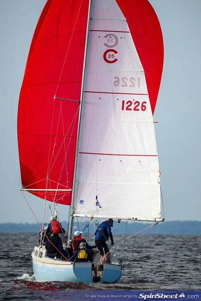 Sailing yacht with a red and white spinnaker sail on open water with four crew members on board