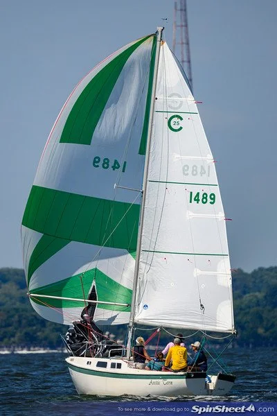 Sailboat with green and white sails on the water, with three people on board.