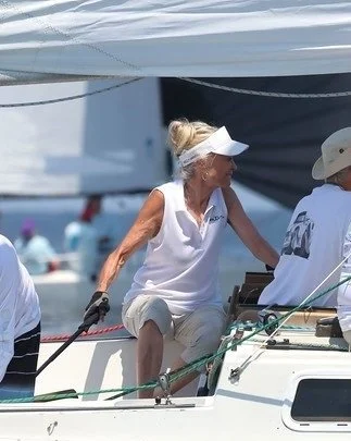 Woman with blonde hair wearing a white visor, sleeveless white shirt, and khaki shorts on a boat, holding a rope.
