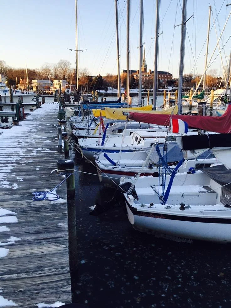 Boats docked at a marina with snow on the pier on a winter day.
