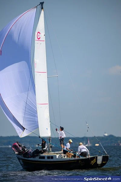 Four people sailing a large sailboat with a prominent white sail on the water during daytime.