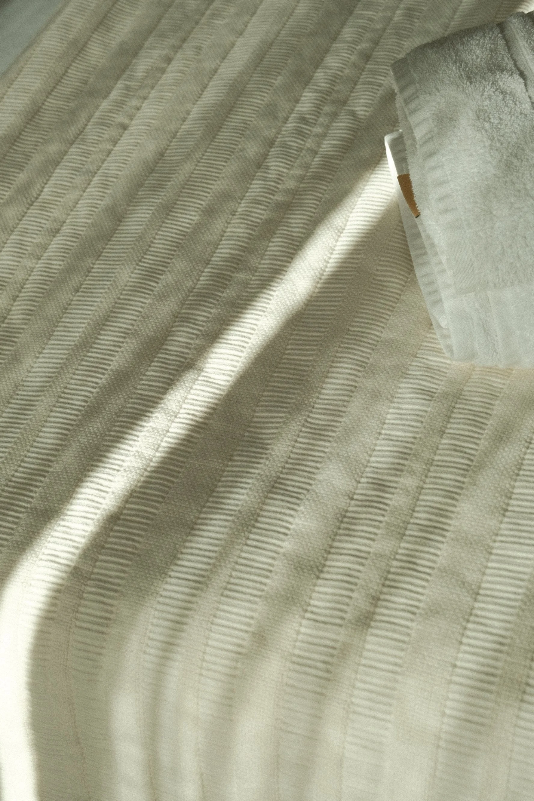 A close-up of a bed with striped beige and cream bedding and a neatly folded white towel on top.