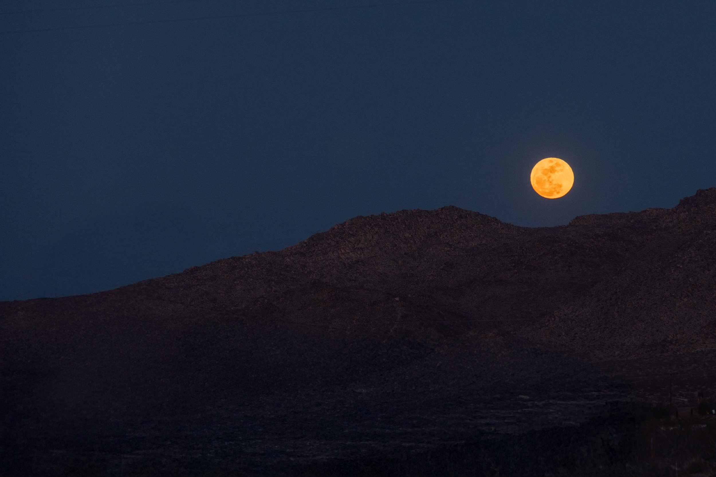 A bright orange full moon rising behind dark mountain ridges against a dark night sky.