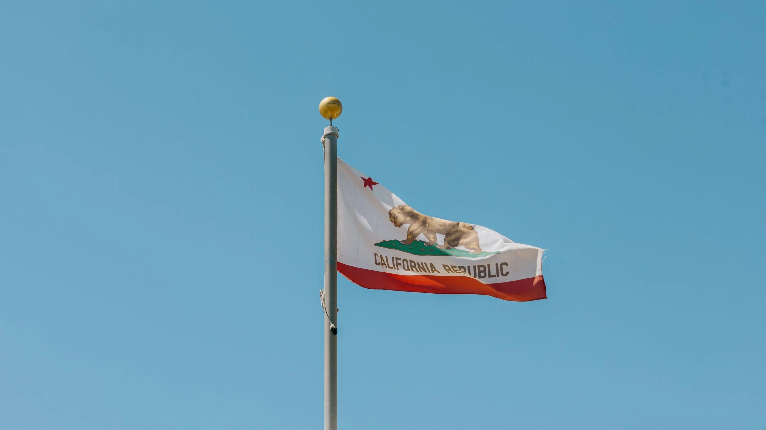 California state flag waving in the wind against a clear blue sky.