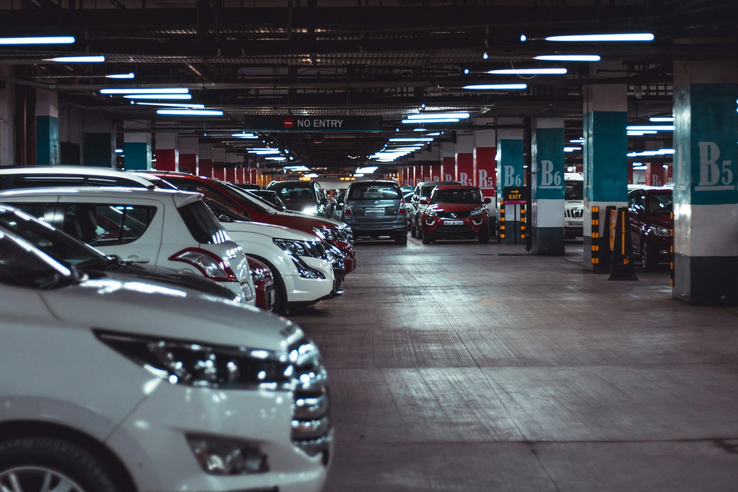 Underground parking garage filled with parked cars, illuminated by ceiling lights, with a no entry sign hanging from the ceiling.