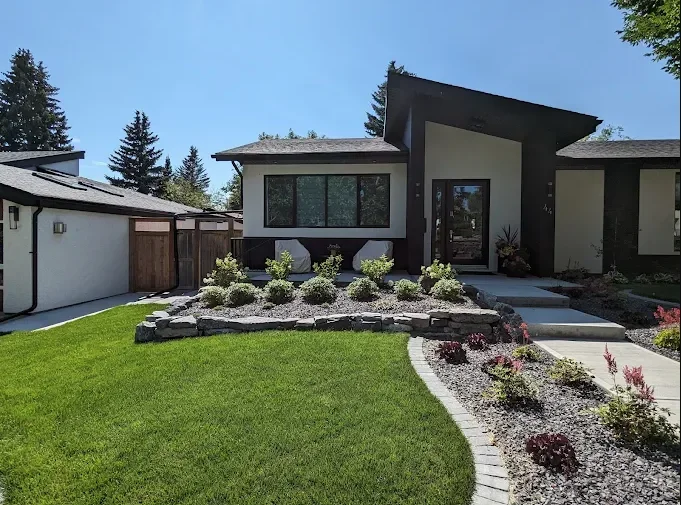 Modern house with a landscaped front yard, green lawn, and a curved pathway leading to the entrance, under a blue sky with some trees in the background.