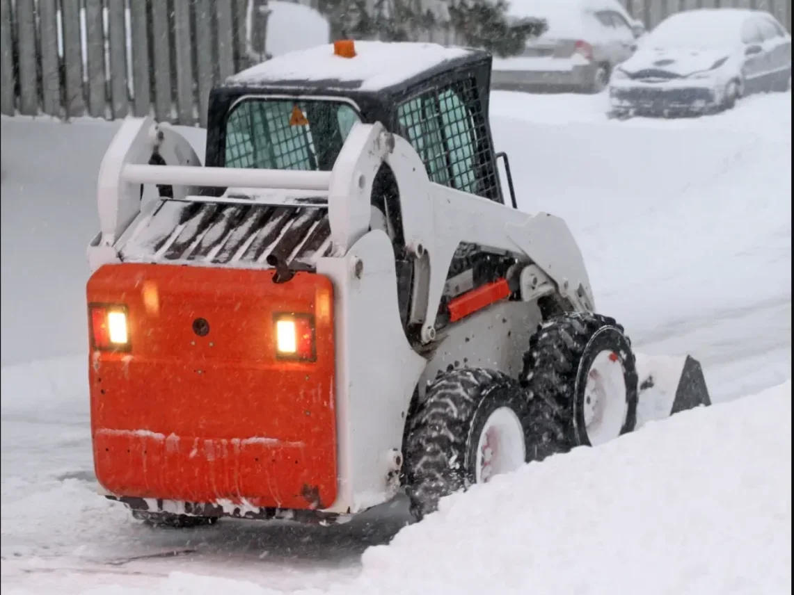 A skid steer clearing snow from a city street in winter.