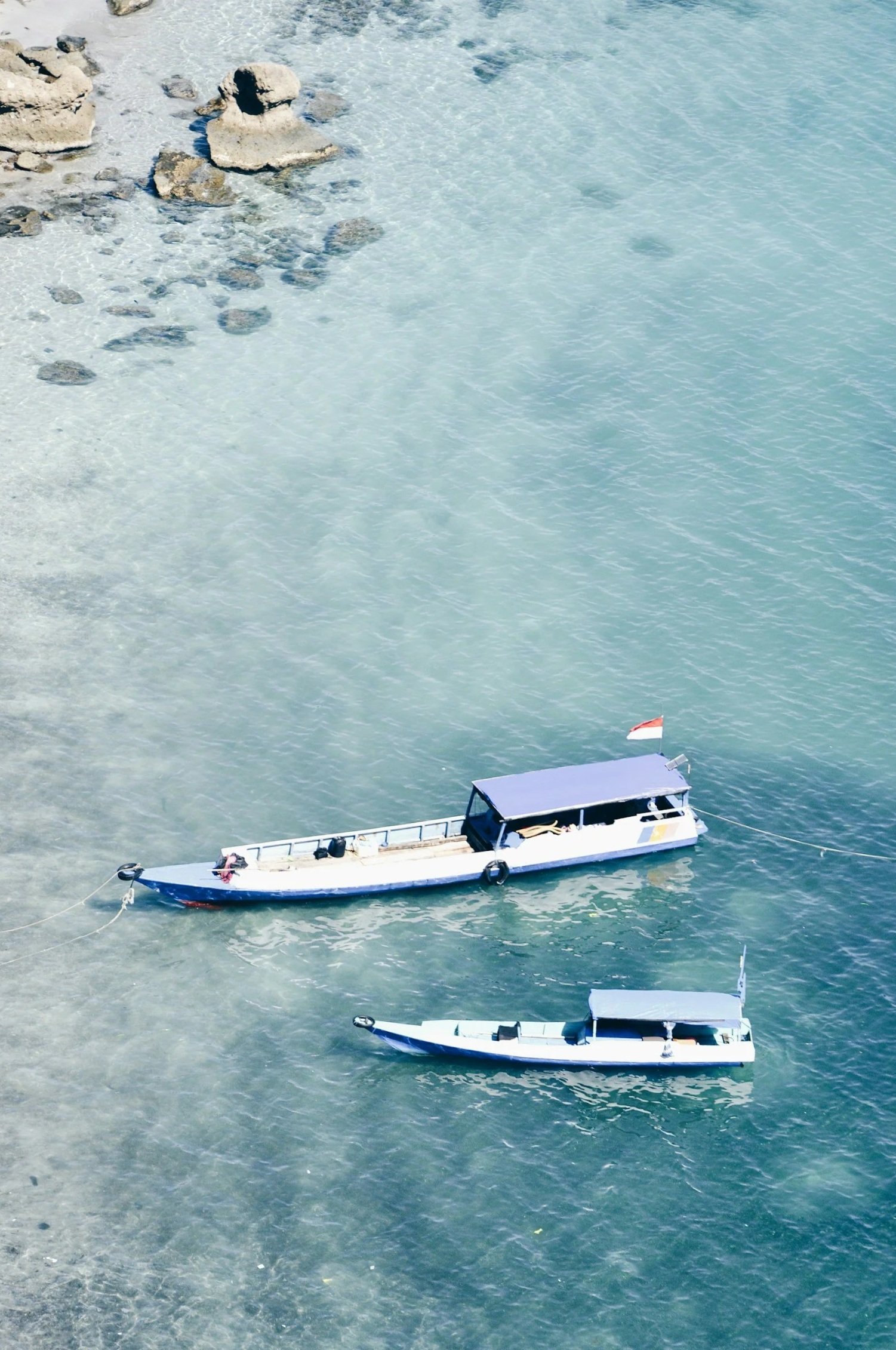 Two boats floating in clear, turquoise water near a rocky shoreline.