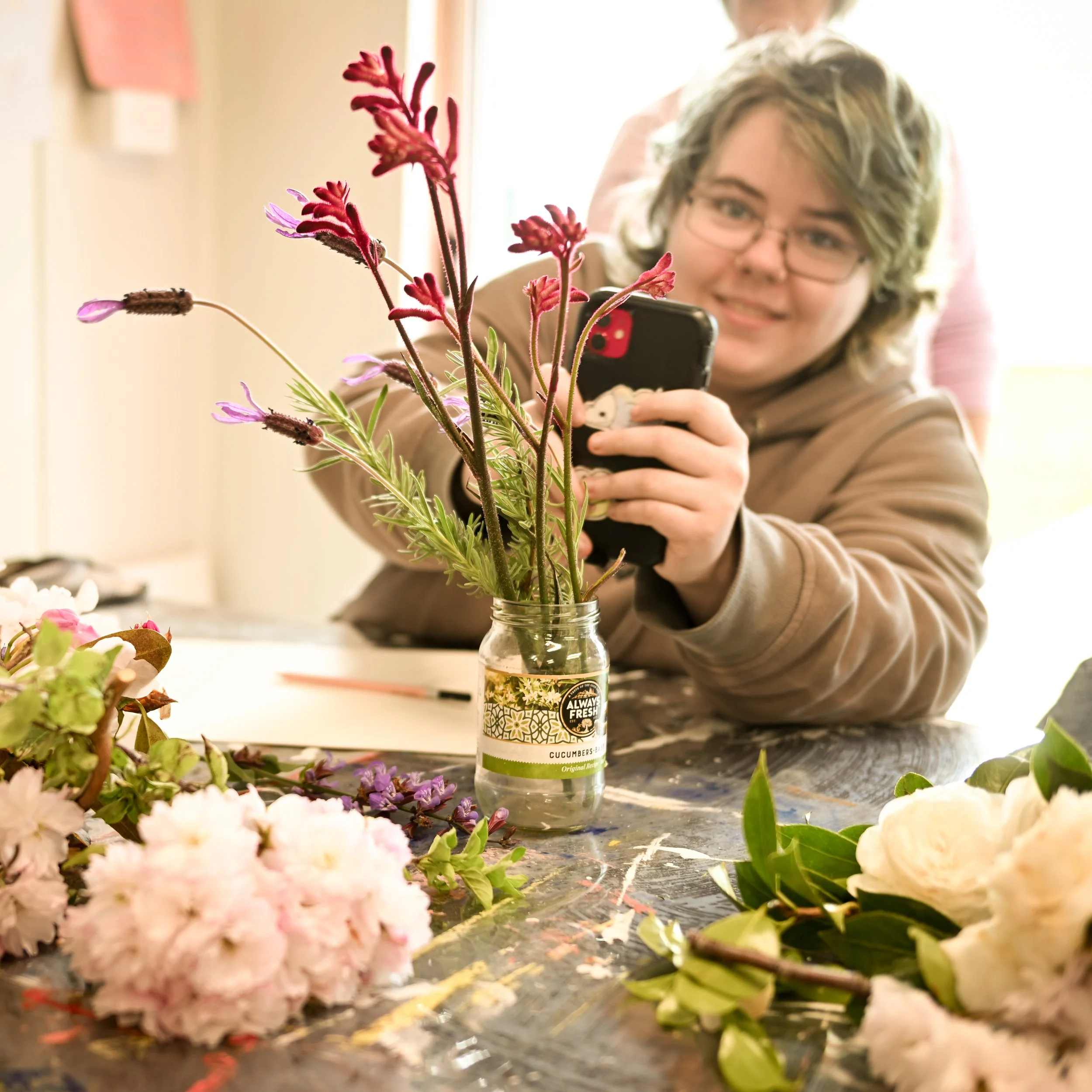 Artist Byanka Franey takes a photo with her iphone of kangaroo paw and lavender in a vase on the table.