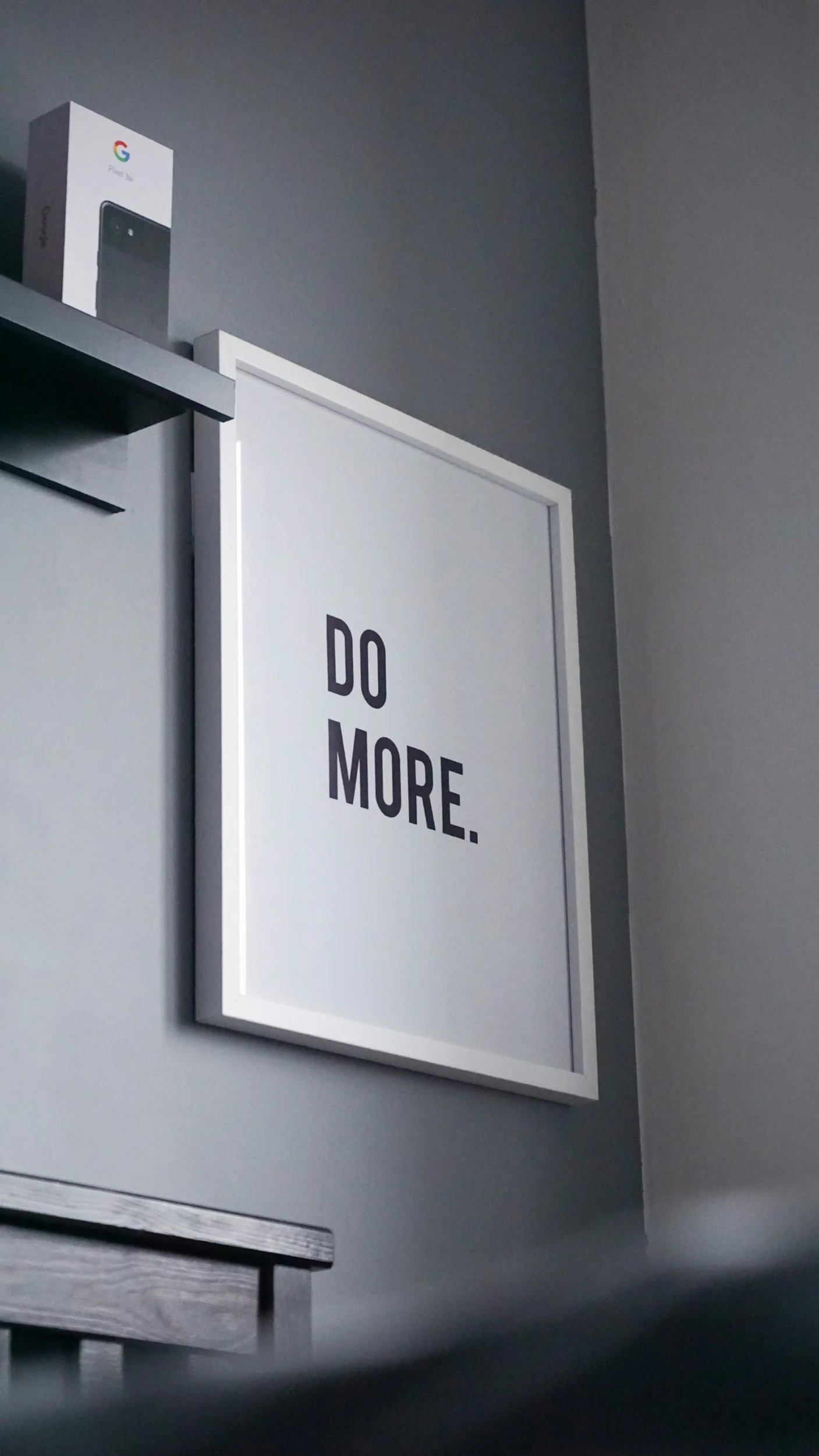 A framed poster on a gray wall with the text "DO MORE." in bold black letters.