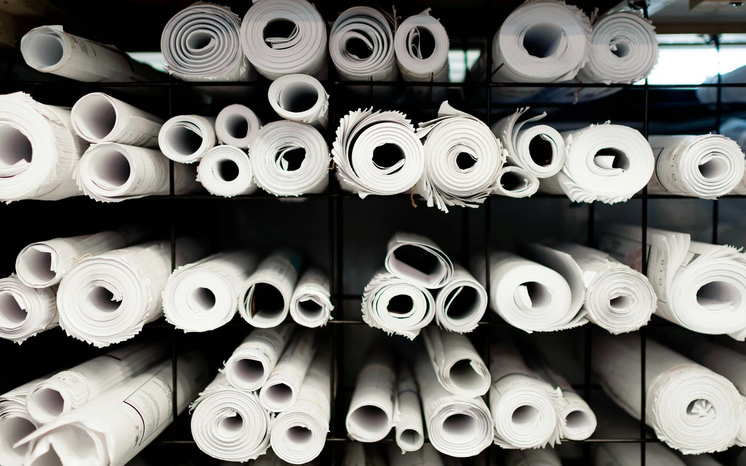 A shelf filled with neatly organized, rolled-up white blueprints or large sheets of paper.