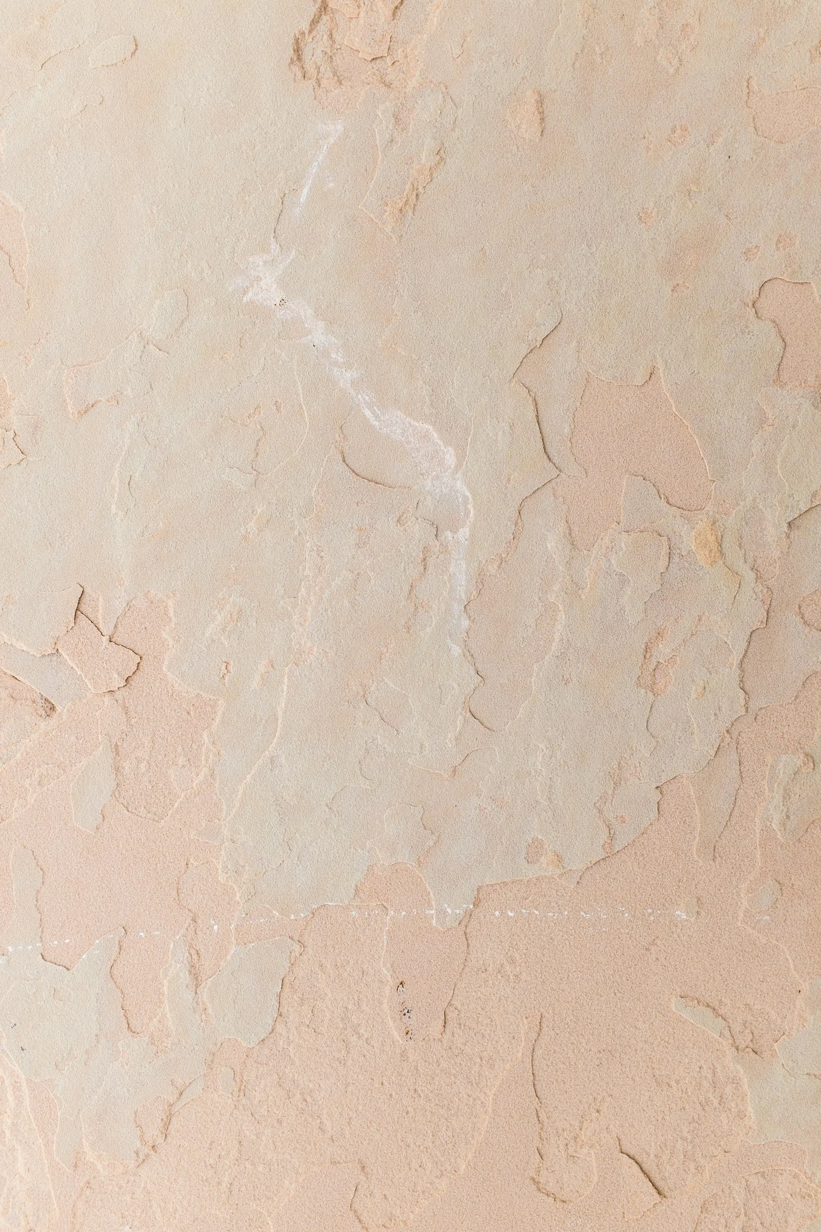 Peeling beige painted wall with cracks and textured surface.