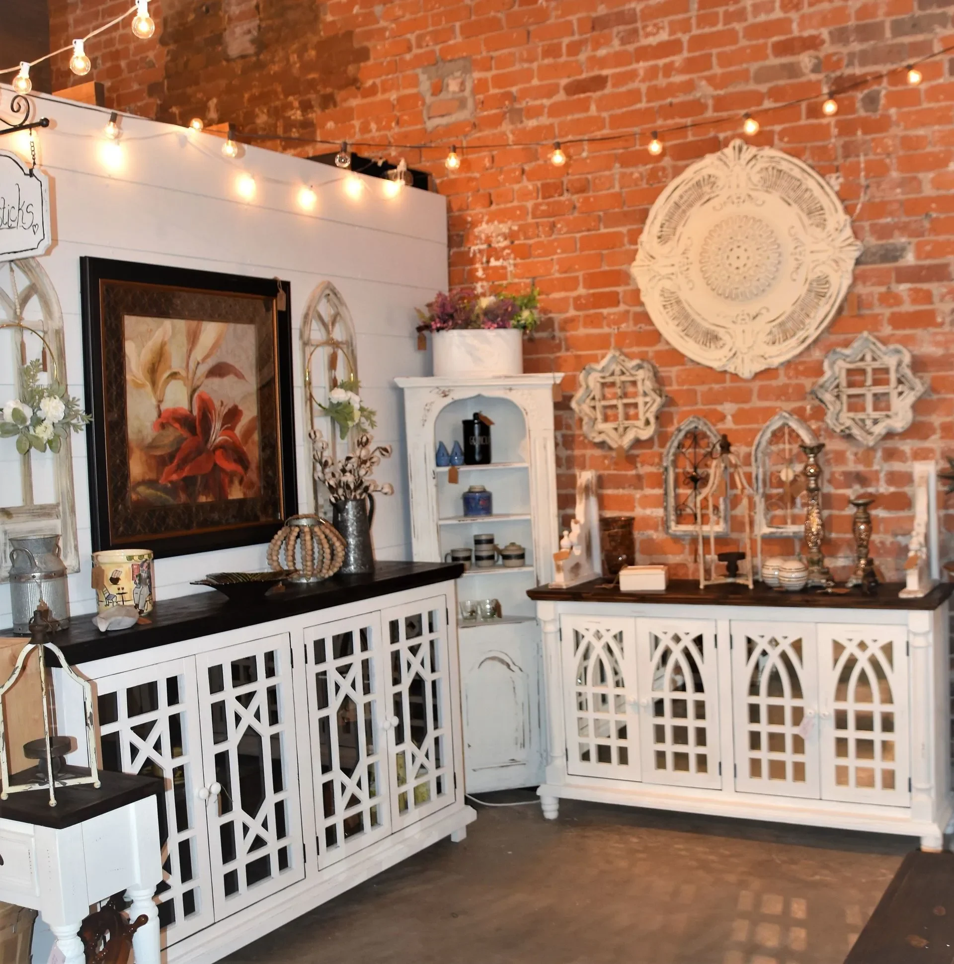 Decorative furniture and wall art in a rustic-style room with exposed brick walls and string lights.