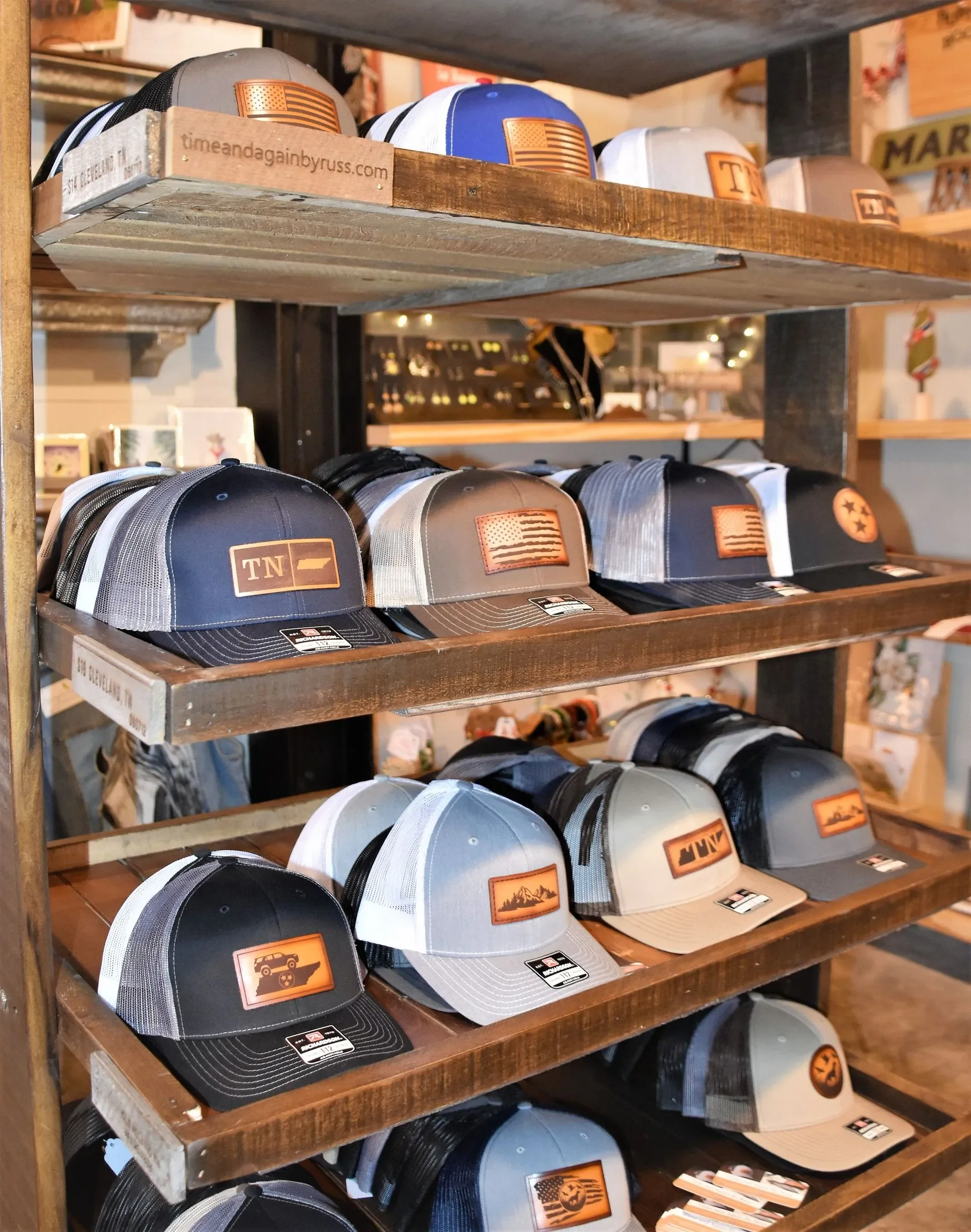 Multiple trucker hats with various patches and logos displayed on wooden shelves in a retail store.