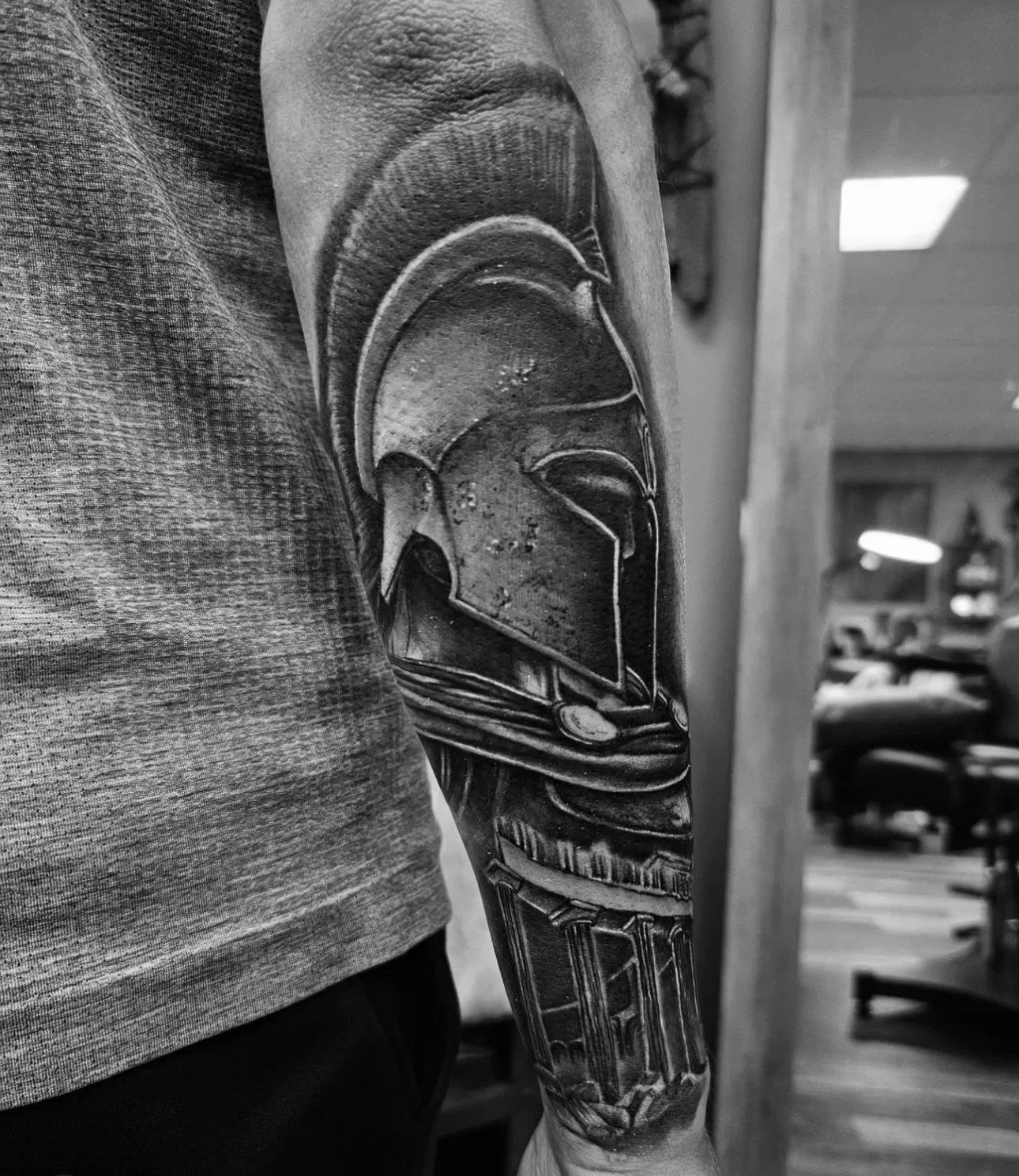 Black and white tattoo of a Spartan helmet on a person's arm.