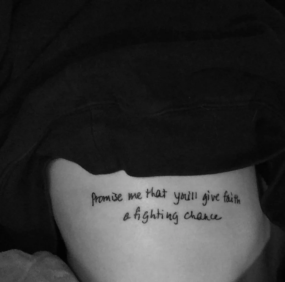 A close-up of a person's stomach with a tattoo that says, 'Promise me that you'll give faith a fighting chance.'