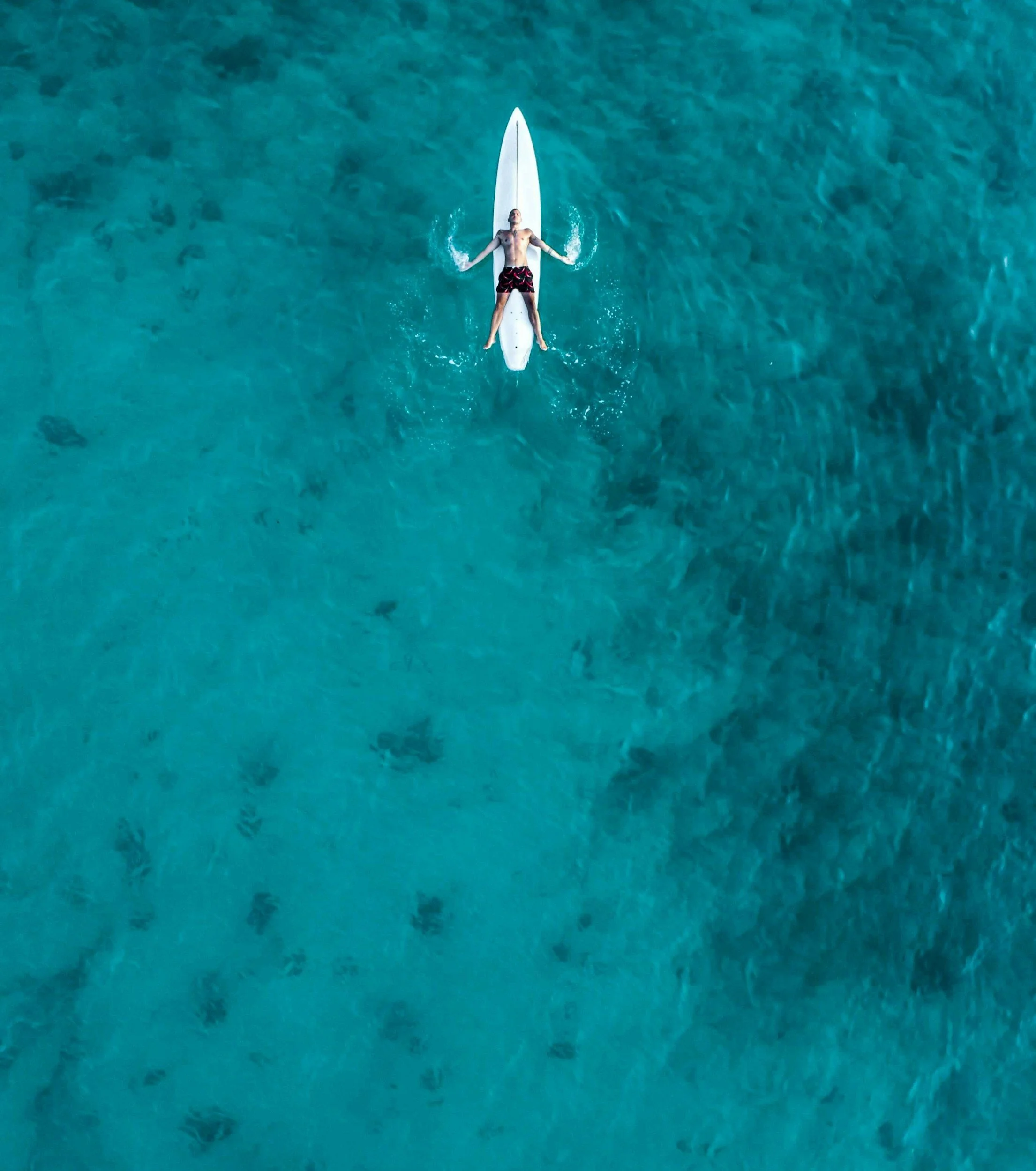 A man lying on a paddleboard on clear blue-green water.