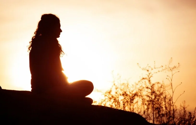 Silhouette of a woman sitting cross-legged outdoors at sunset