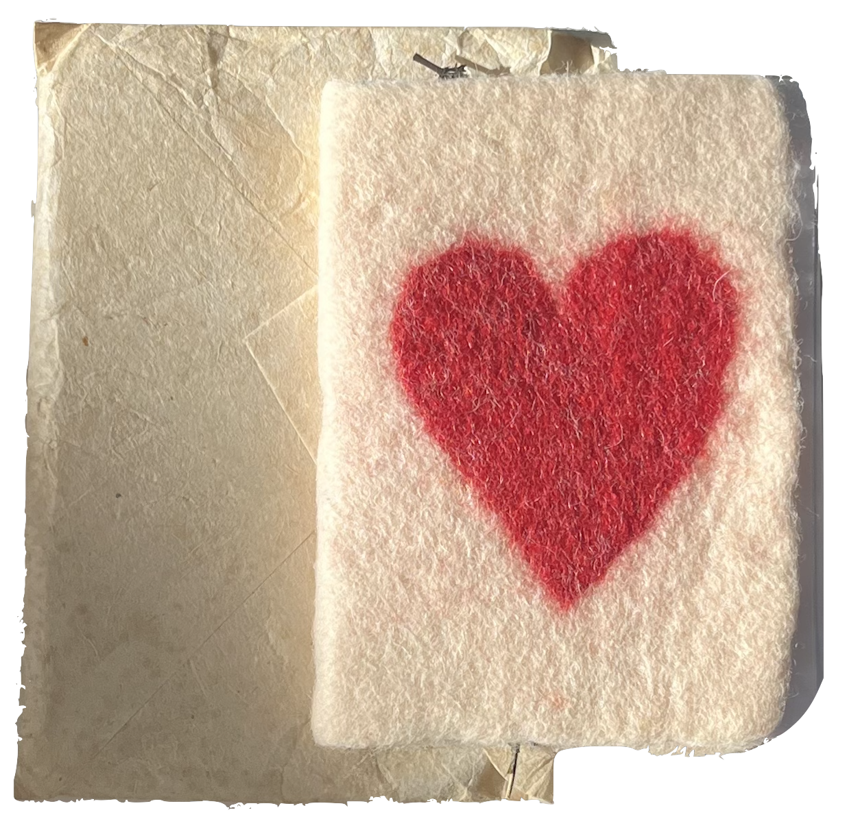 A piece of white felt with a red heart painted on it, placed on a crumpled piece of parchment paper.