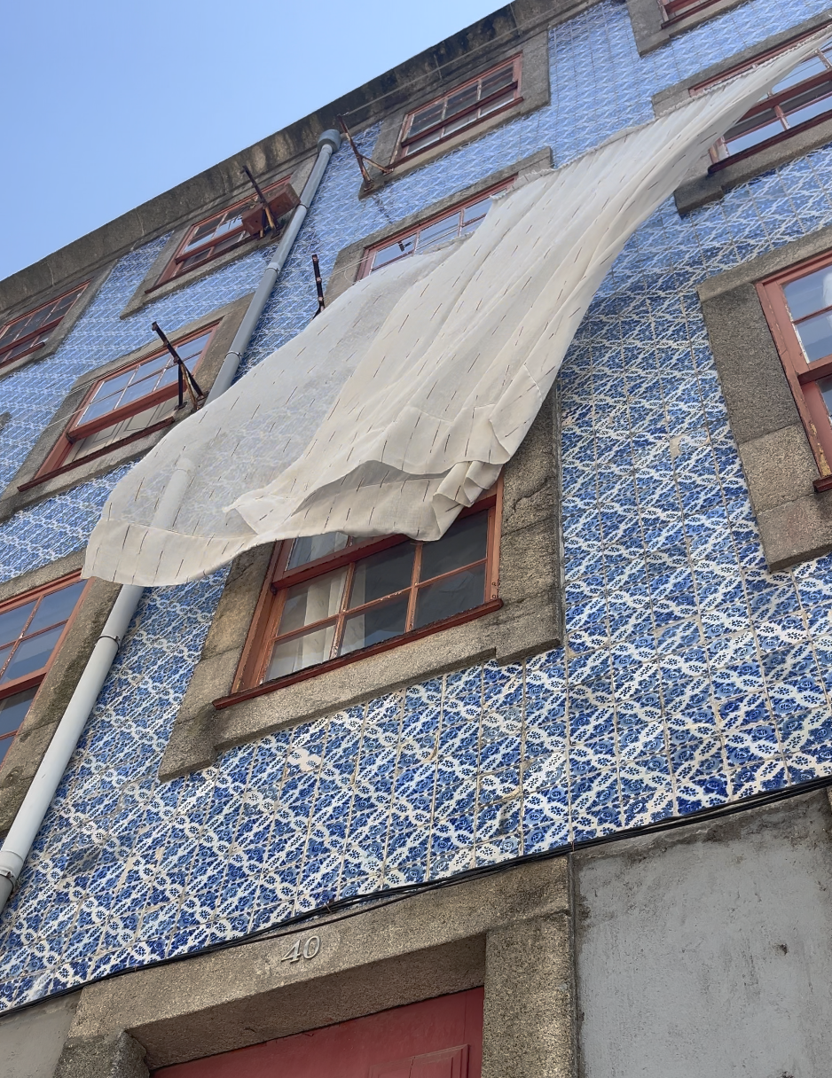Building with blue and white decorative tiles, red window frames, and a beige fabric drape hanging from scaffolding.