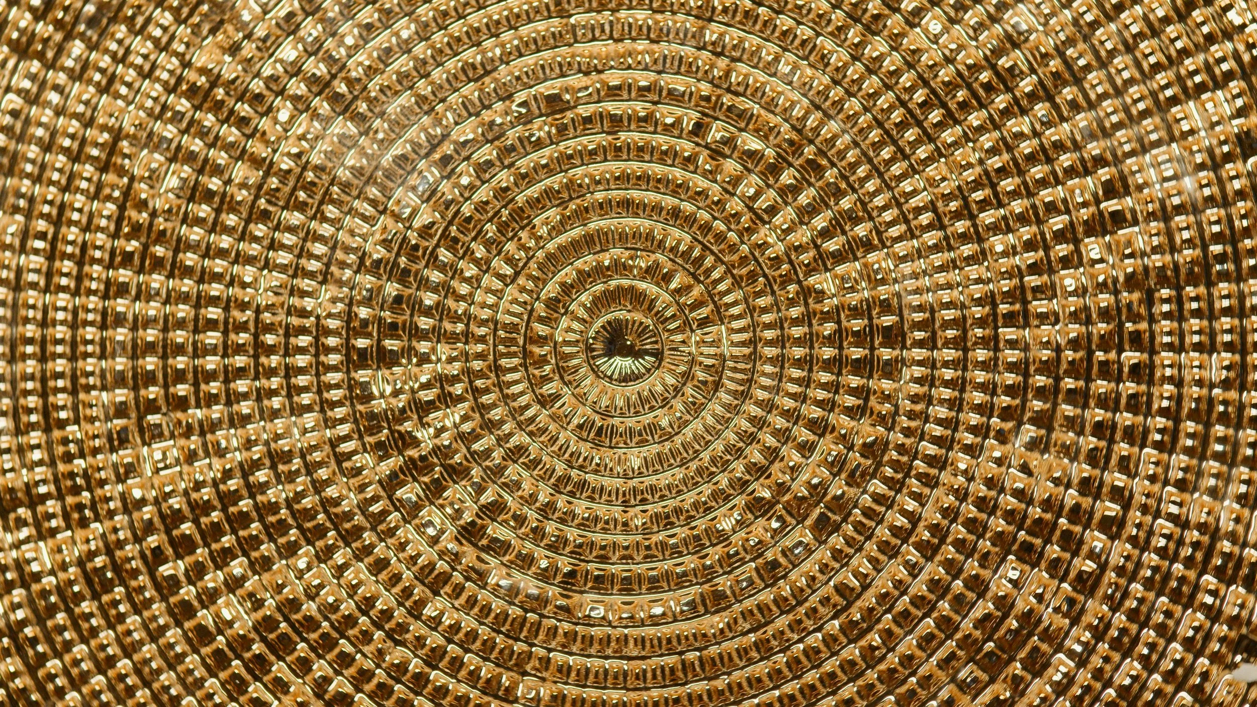 A close-up view of a gold, circular, mosaic-style structure with concentric rings of tiny gold blocks creating a spiral pattern.