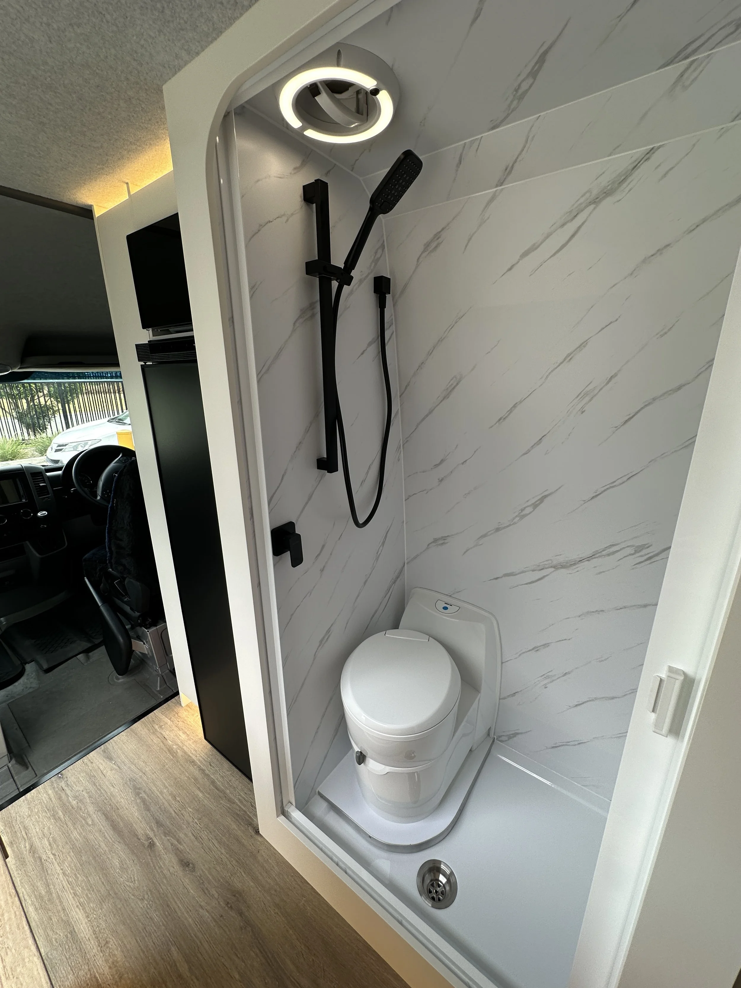 Compact bathroom with a white toilet and a black shower head and handheld shower on a marble-patterned wall.