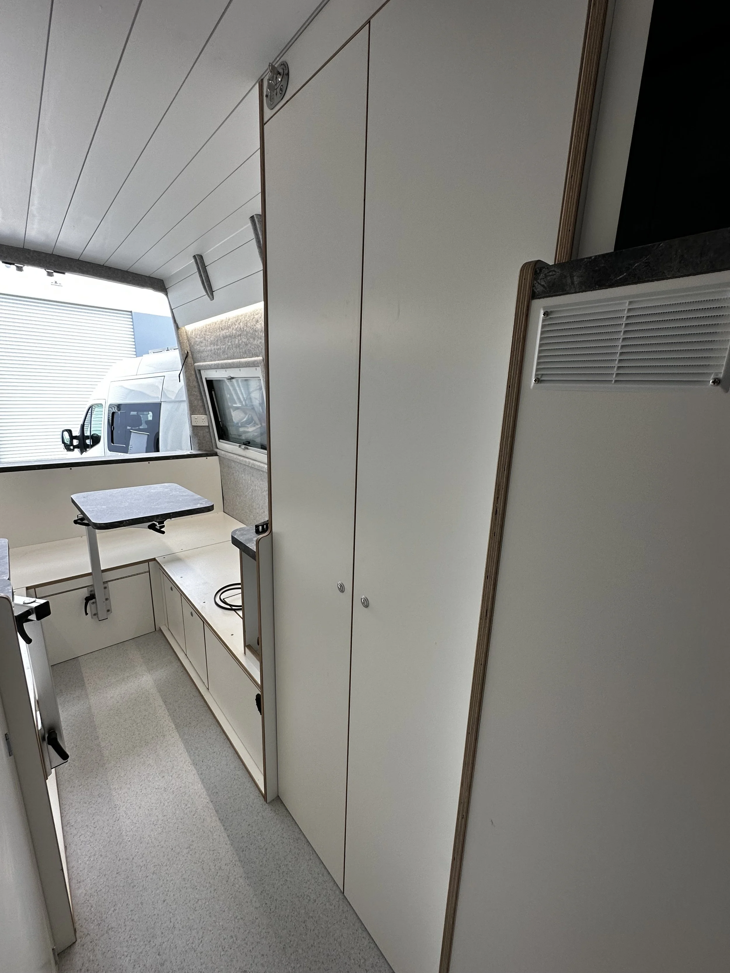 Interior of a small van or camper with white cabinets, a small table, and a window.