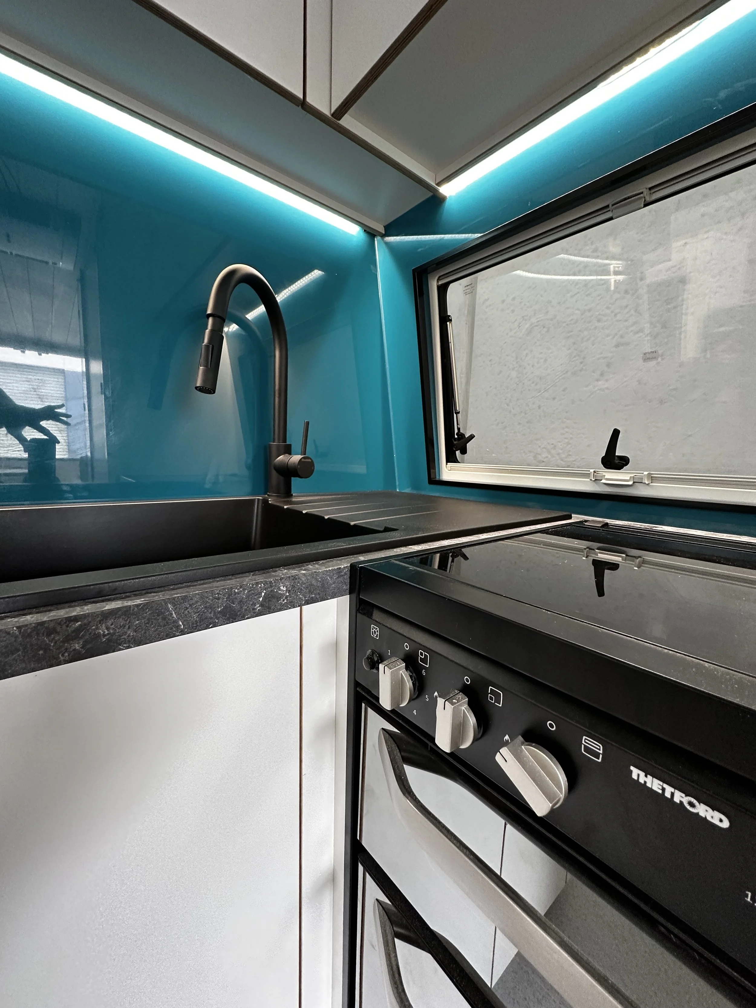 Kitchen with black sink, black countertop, blue wall, black faucet, window, and a black stove.